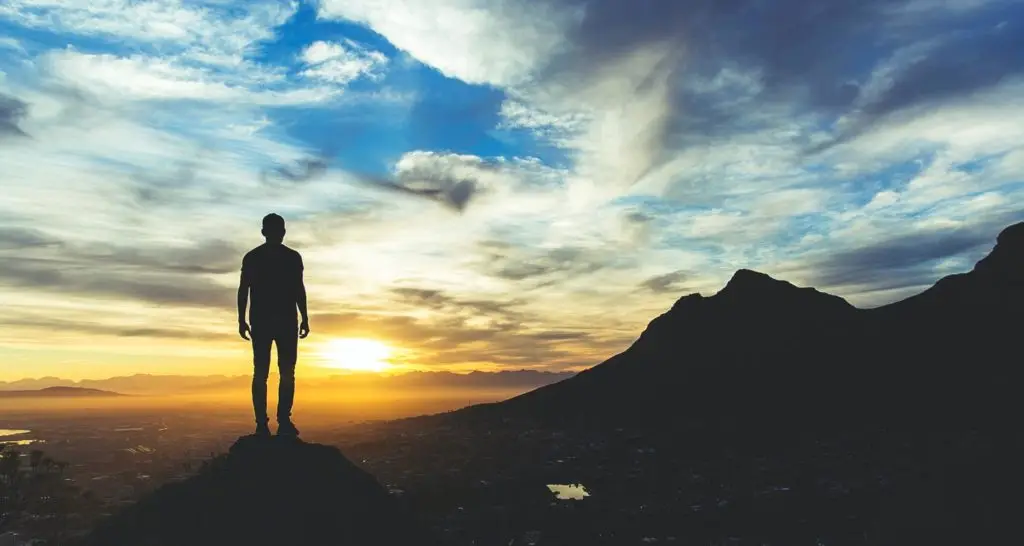 Outline of a man standing on a mountain looking over a city during sunset